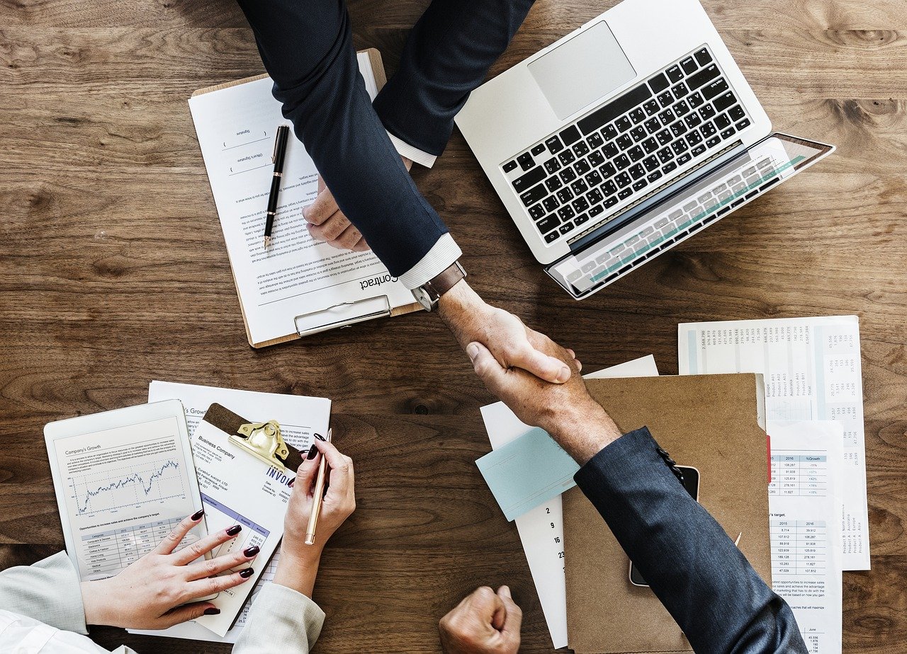 People shaking hands across a desk that has computer and papers on it