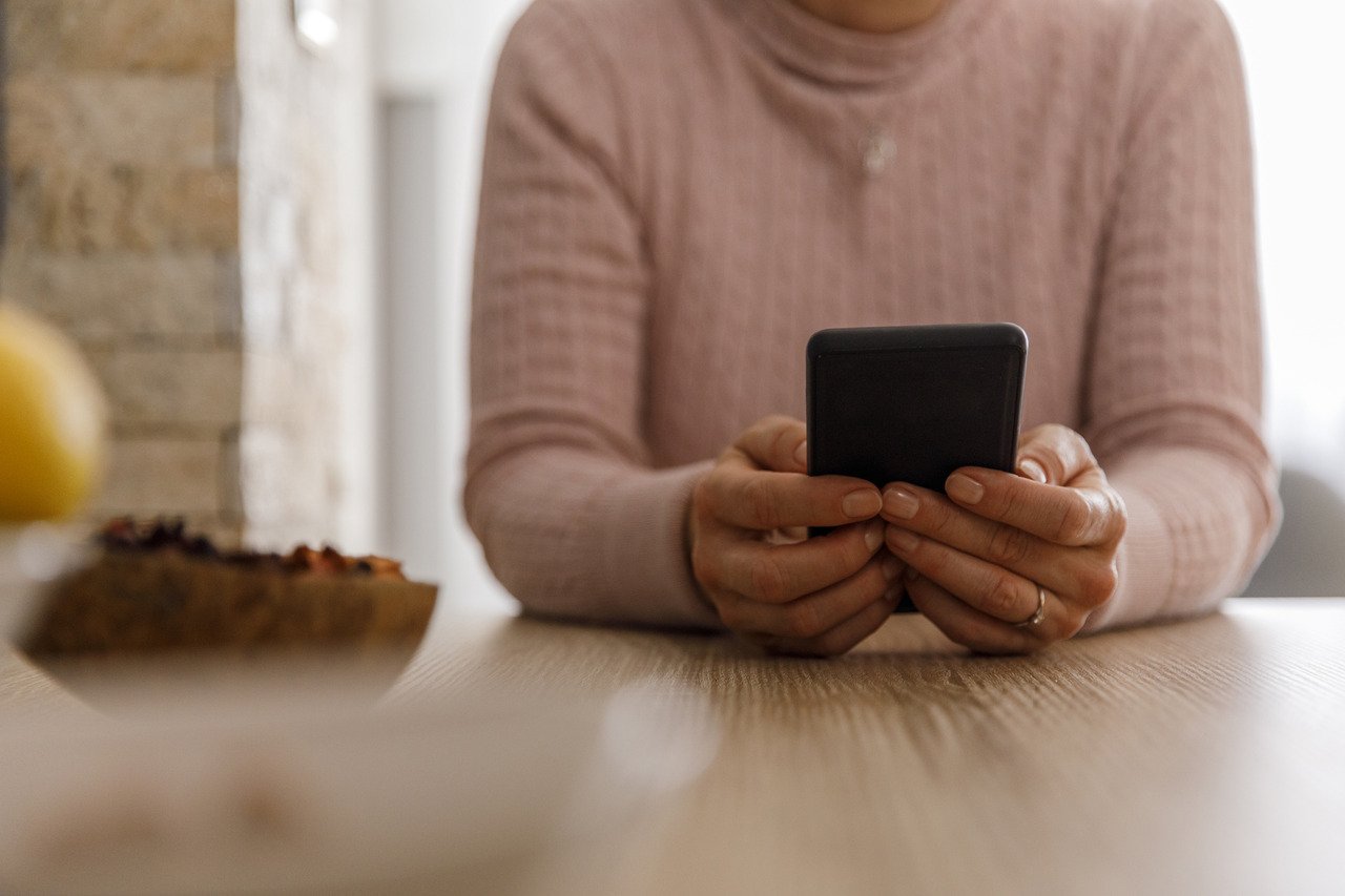 Front view of unrecognizable mature woman sitting at the table and typing a text message on her smart phone