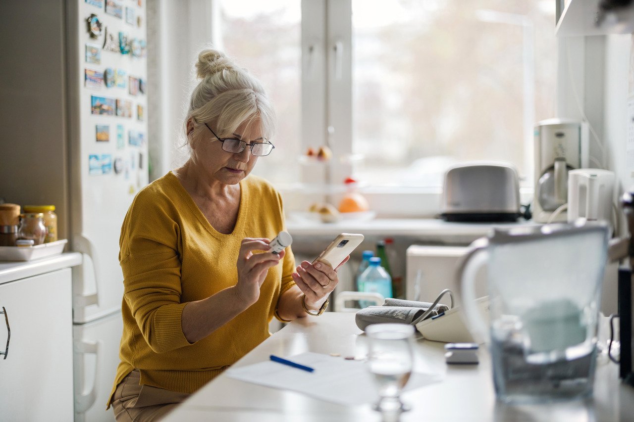 older woman in kitchen checking prescription on smartphone