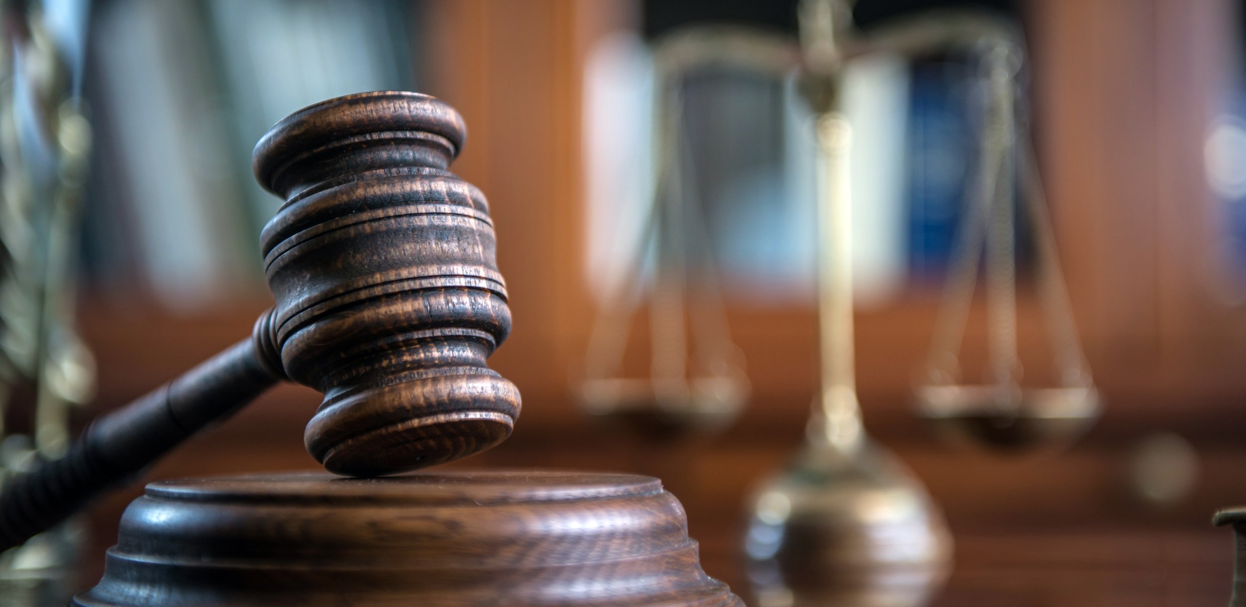 A gavel in the foreground with the scale of justice in the background