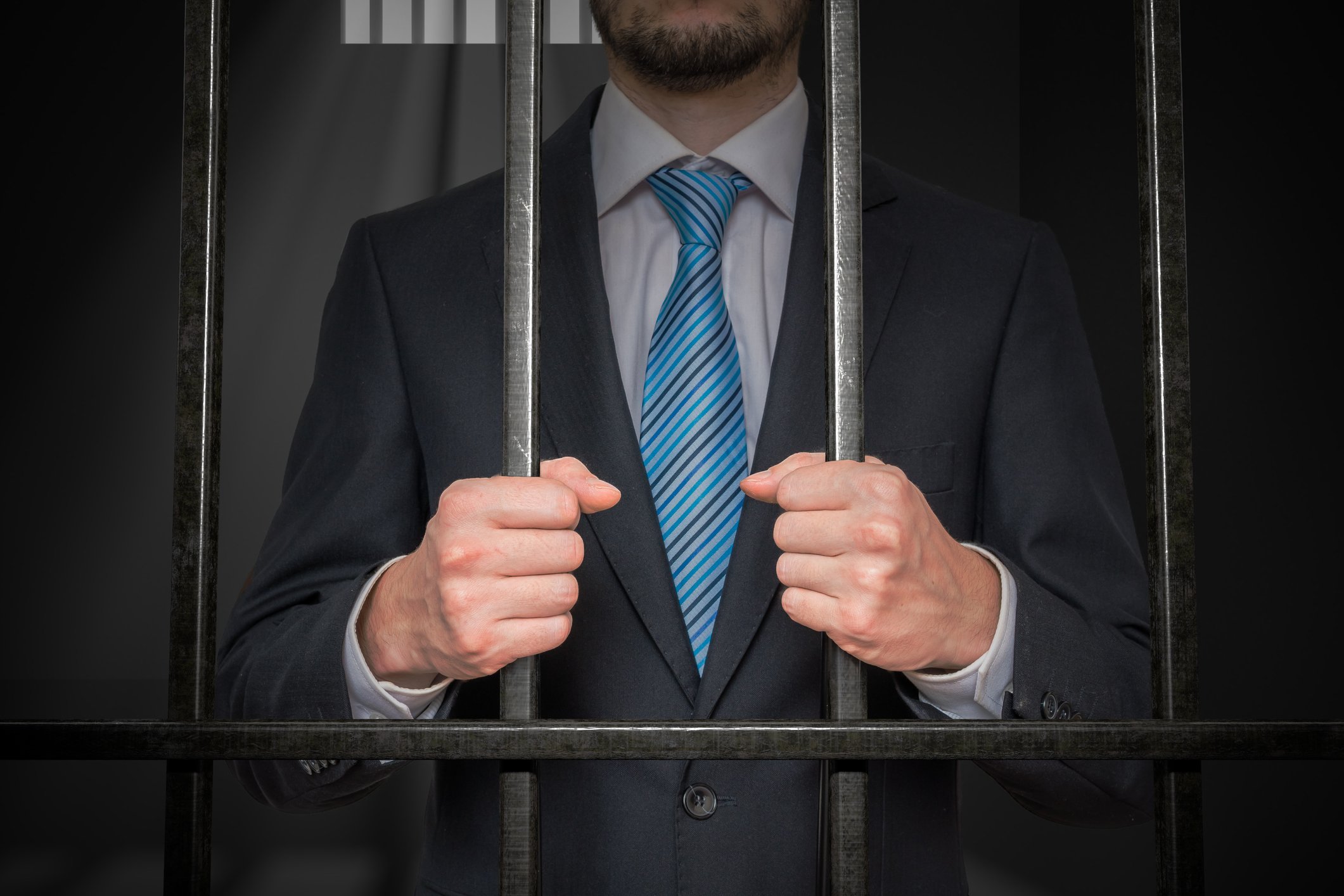 Businessman or politician with handcuffs behind bars in prison cell